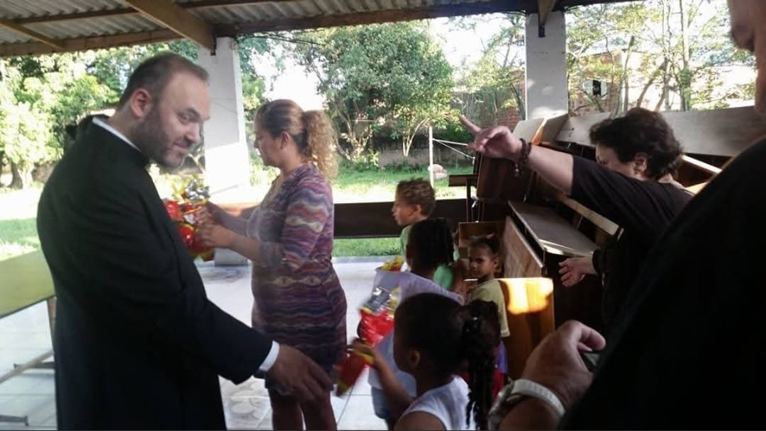Sacerdote entrega presentes às crianças na área externa