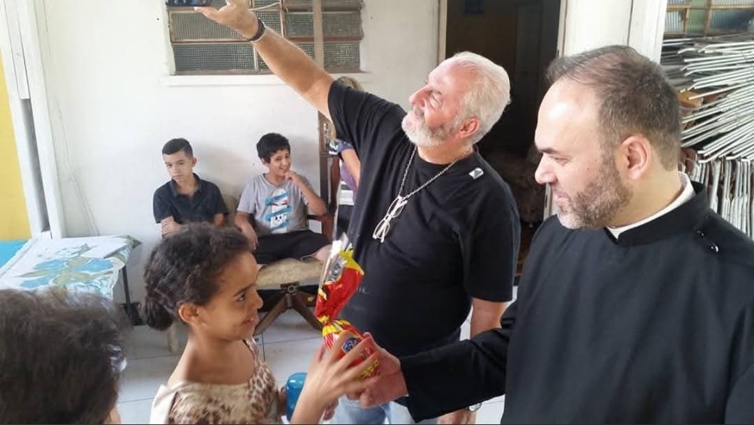 Sacerdote e voluntário entregam presente a uma criança