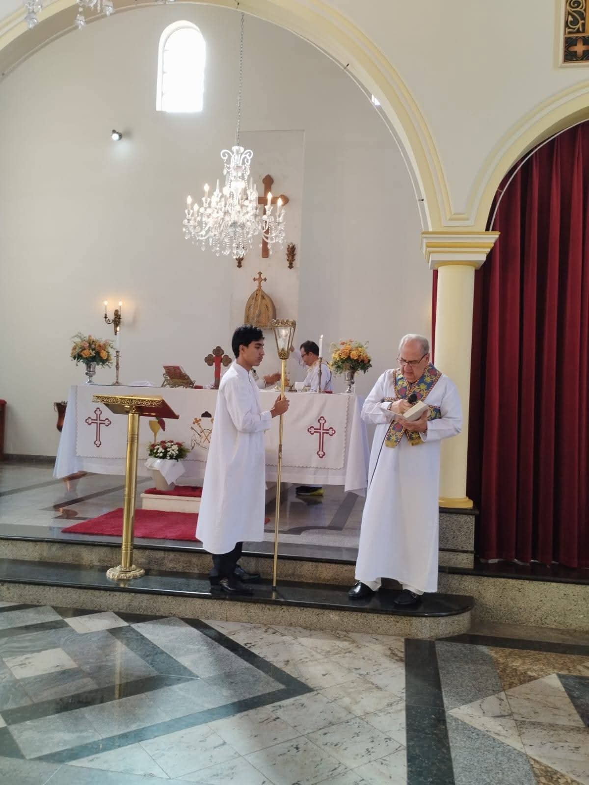 Sacerdote lendo durante a celebração, ao lado de um acólito com lanterna